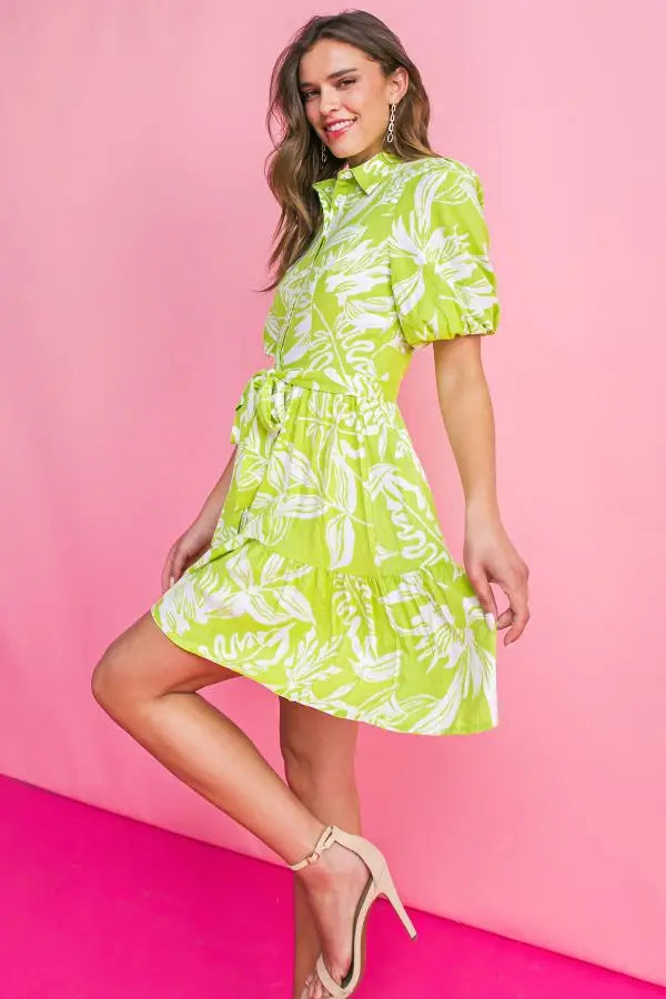 Island time dress. A printed woven mini dress featuring shirt collar, button down, short puff sleeve, self sash tie and ruffled hemline. chartreuse green floral print. 